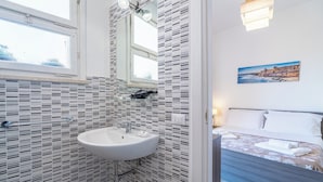A bathroom with a tiled backsplash, a sink, and a window. - Cavour Rooms (Syracuse)