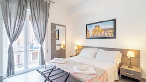 A hotel room with a bed, a nightstand, a lamp, a window with curtains, and a painting on the wall. - Cavour Rooms (Syracuse)