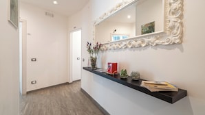 A hallway with a black reception desk, a mirror with an ornate frame, and a door leading to another room. - Cavour Rooms (Syracuse)