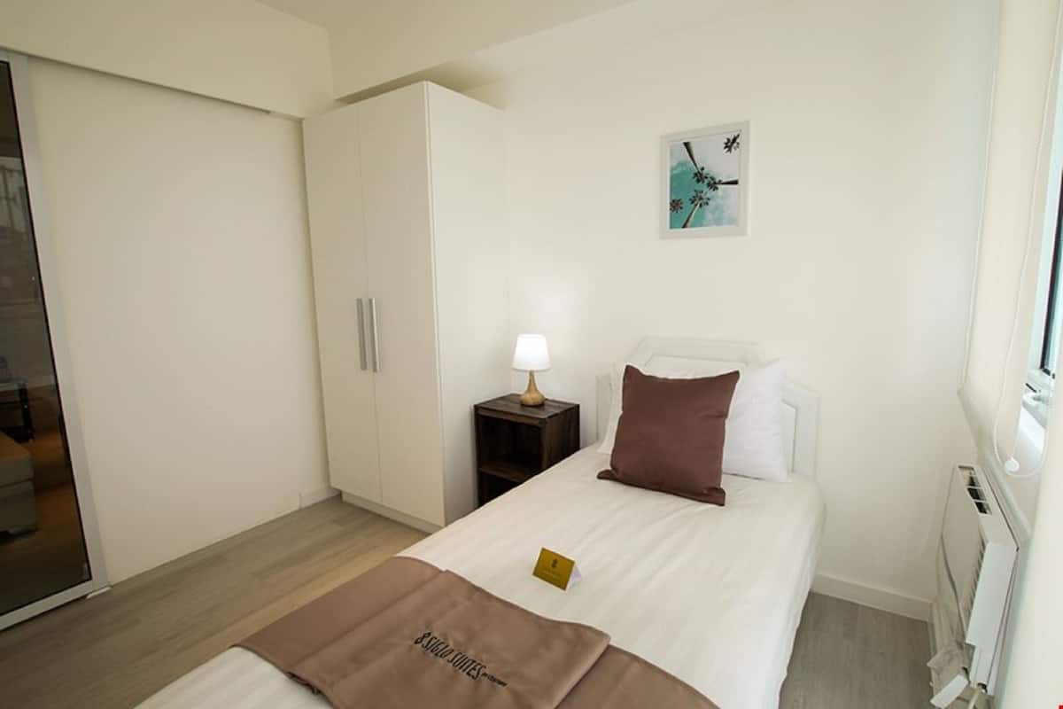 A hotel room with a bed, a nightstand with a lamp, a wardrobe, and a painting on the wall.
