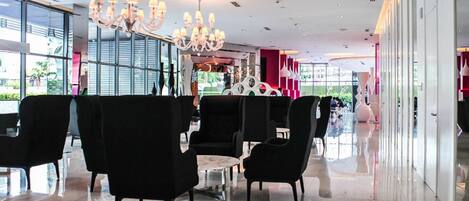 A modern lobby with black upholstered seating, a marble floor, and a large chandelier.