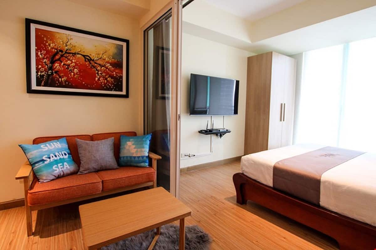A modern hotel room with a sofa, a bed, a TV, and a painting on the wall.
