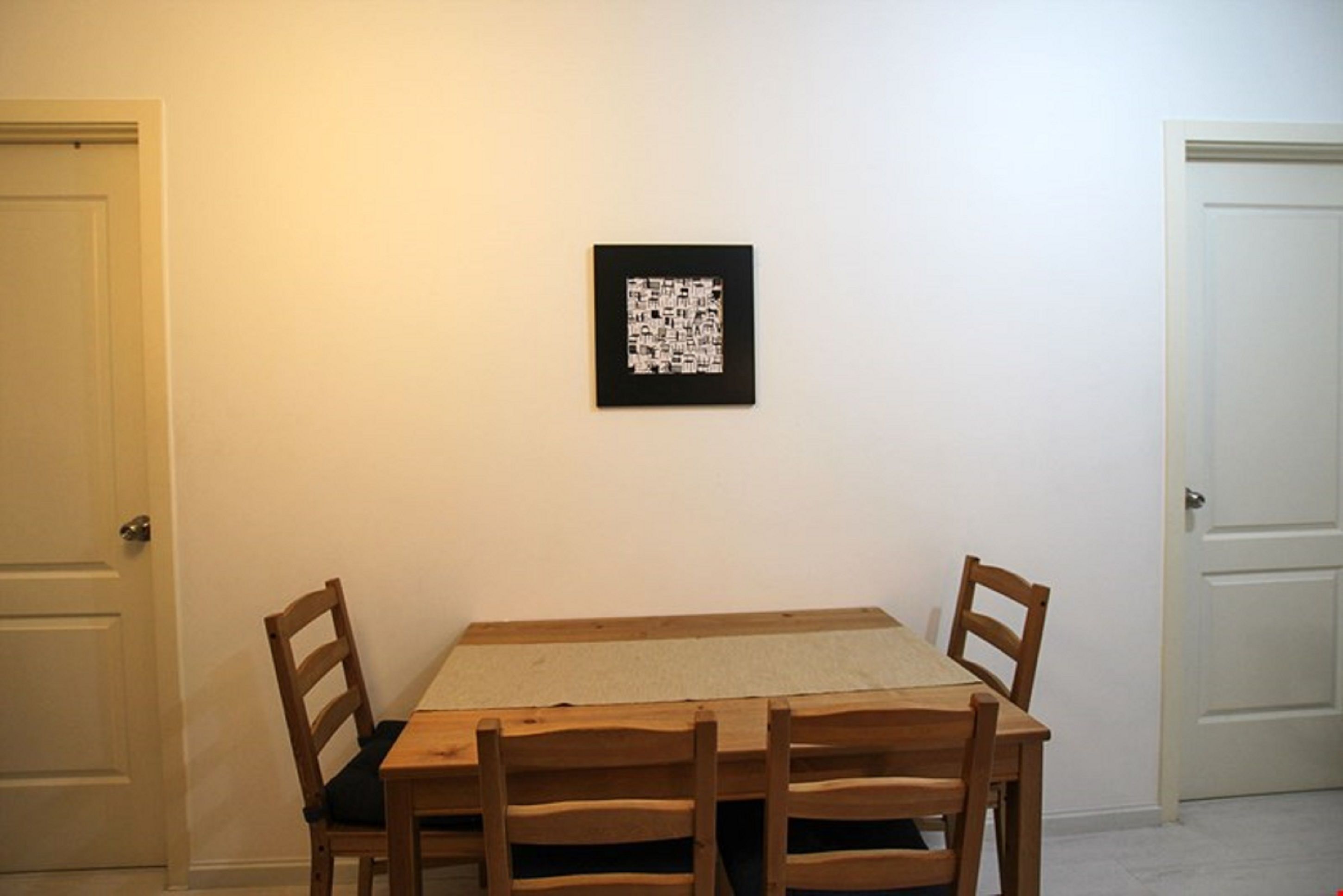 Un coin repas avec une table en bois et quatre chaises, un tableau encadré au mur et deux portes.