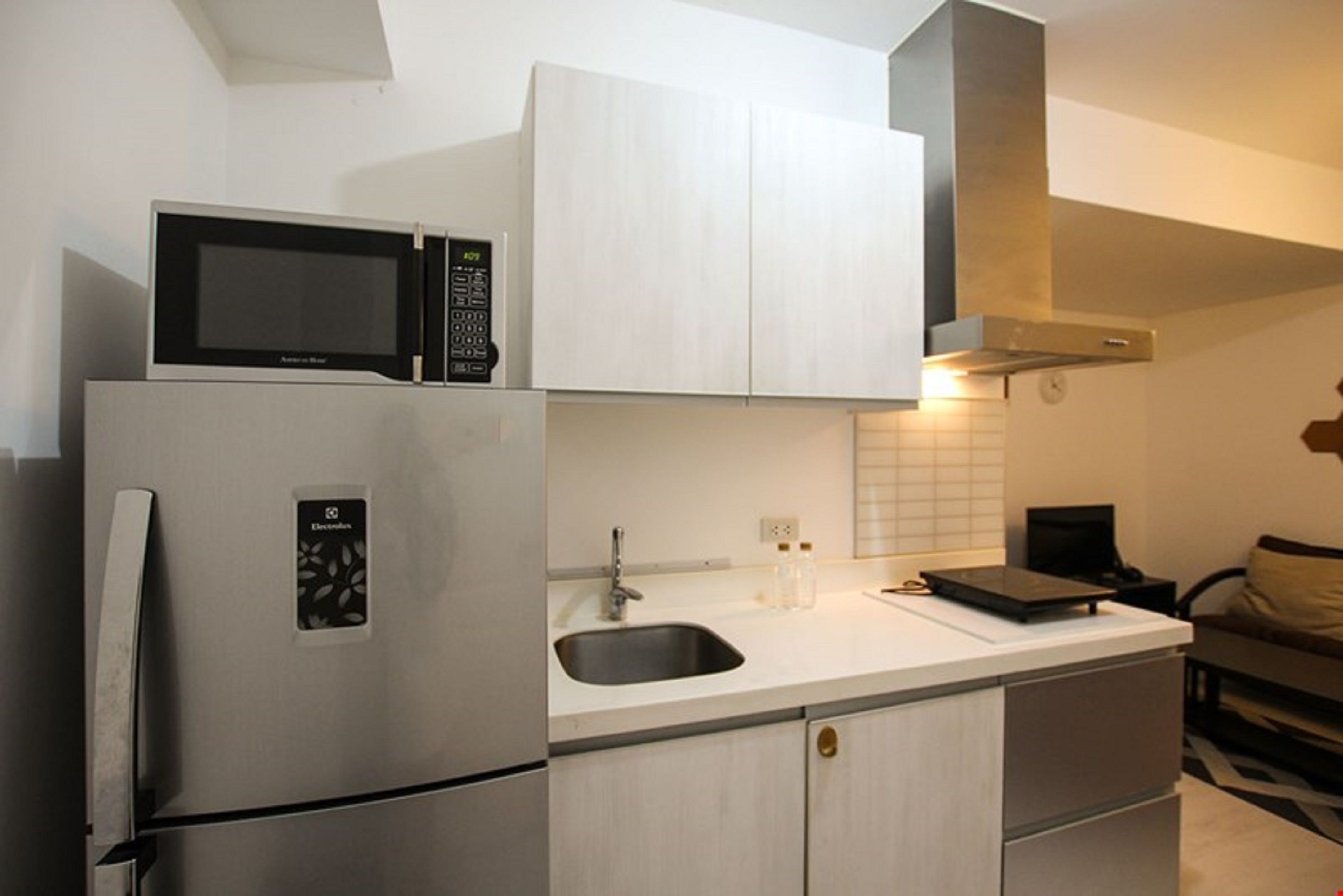 A compact kitchen with a built-in microwave, a stainless steel refrigerator, a sink, and a countertop with a tablet and bottles.