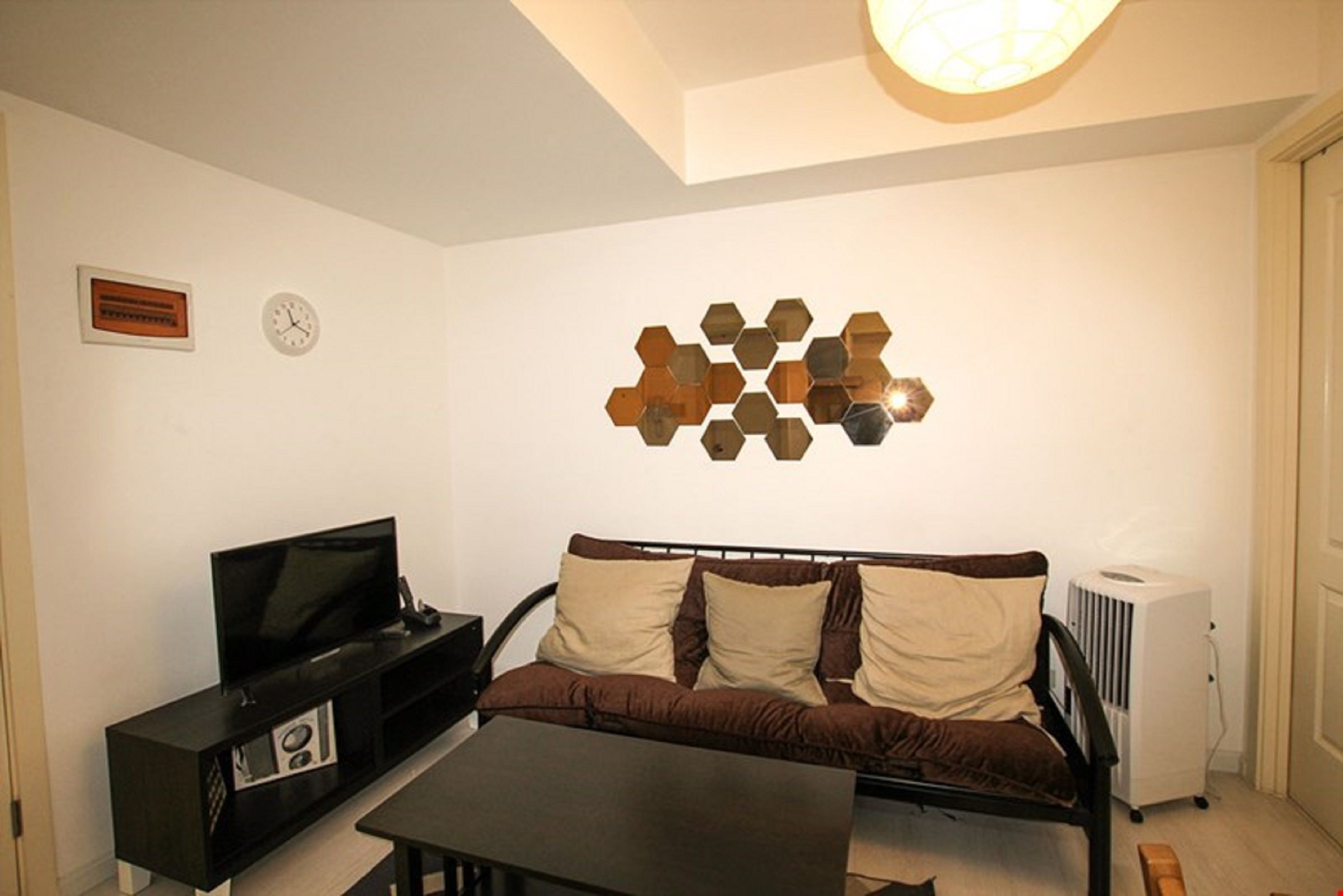 A living room with a sofa, a TV, a coffee table, a wall clock, and a decorative hexagonal wall piece.