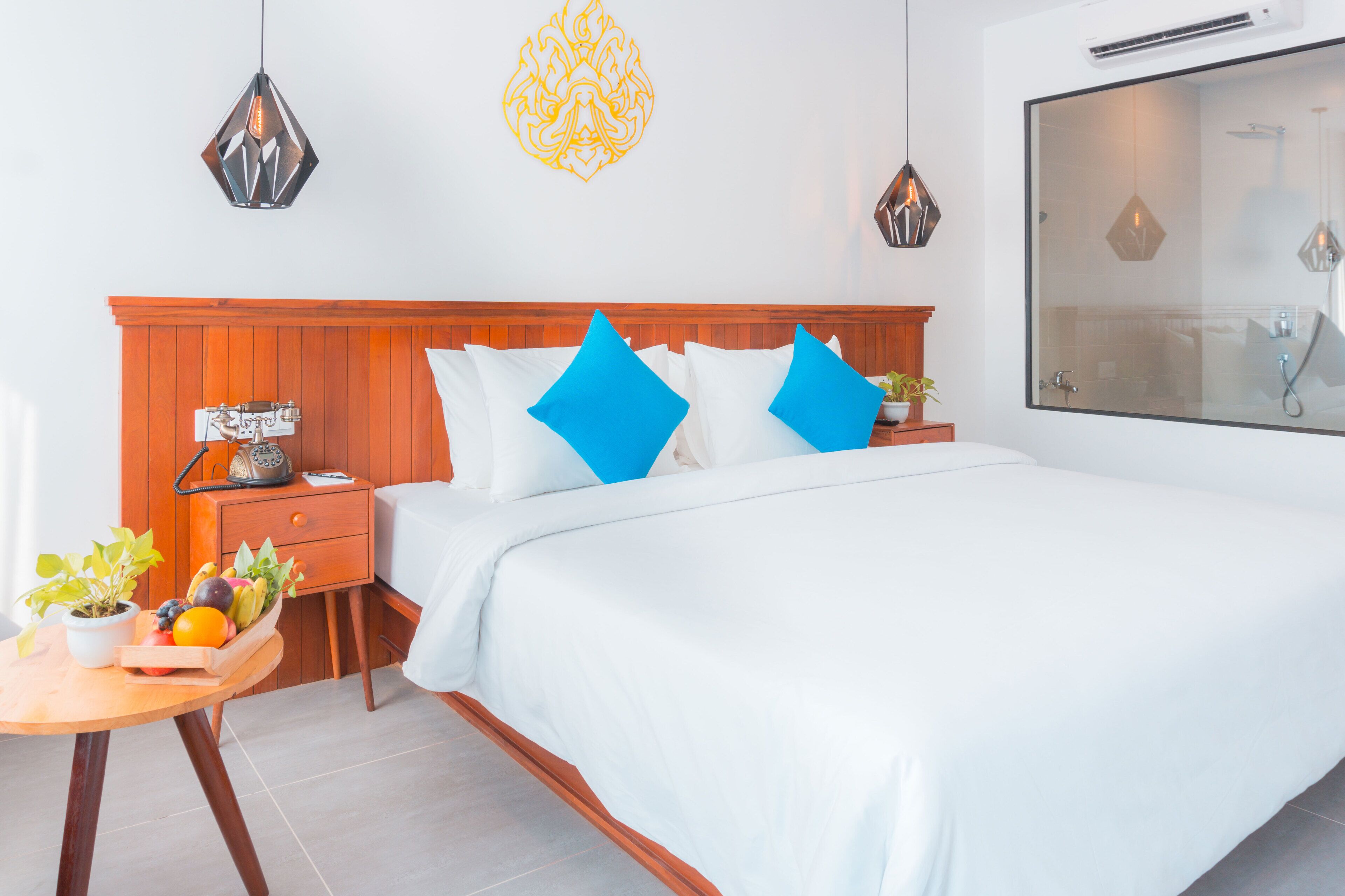 Een moderne hotelkamer met een houten hoofdeinde, witte beddengoed en een fruitmandje op een bijzettafeltje.