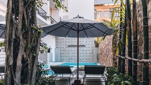Zona de piscina con dos sillas reclinables, un toldo grande y una pared de piedra.