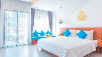 A hotel room with a large bed, blue pillows, a wooden headboard, a hanging light fixture, and a view of the city through large windows.