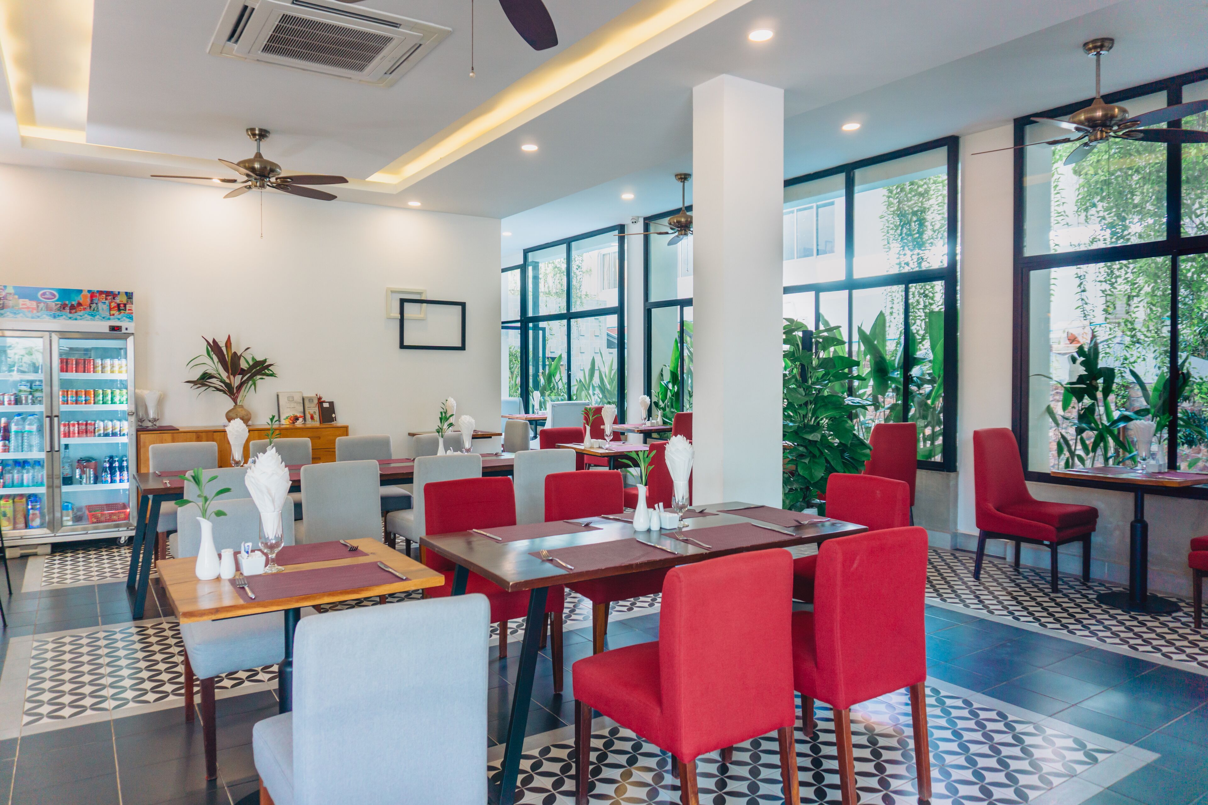Un restaurant moderne avec des sièges rouges et gris, de grandes fenêtres et un ventilateur de plafond.