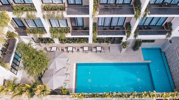 Un hotel moderno con varios balcones, piscina y zonas de estar al aire libre.