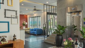 Un vestíbulo de hotel moderno con un sofá azul, un mueble de madera y una mesa con un florero y una botella de vino.