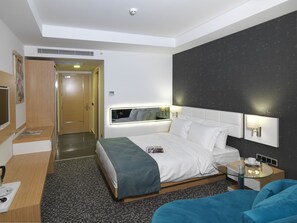 A modern hotel room with a bed, bedside table, and a seating area with a blue sofa.