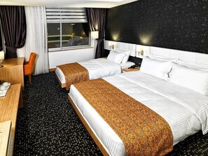 A hotel room with two beds, a desk, a chair, and a window with curtains.