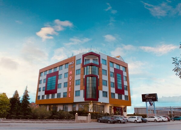 A modern hotel with a prominent "INCI HOTEL" sign, multiple floors, and a parking lot with several cars.