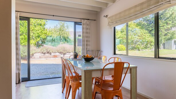 Un coin repas avec une table en verre, des chaises orange et un saladier rempli de fruits.