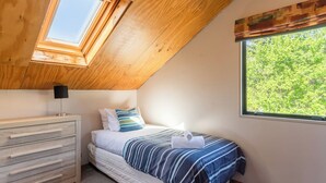 Une chambre avec un puits de lumière, un lit avec une literie à rayures, une table de chevet et une commode.