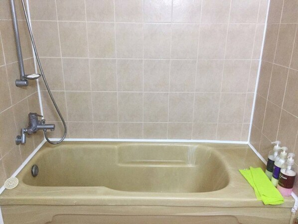 A bathroom with a bathtub, a shower, and a sink. There are toiletries on the sink.
