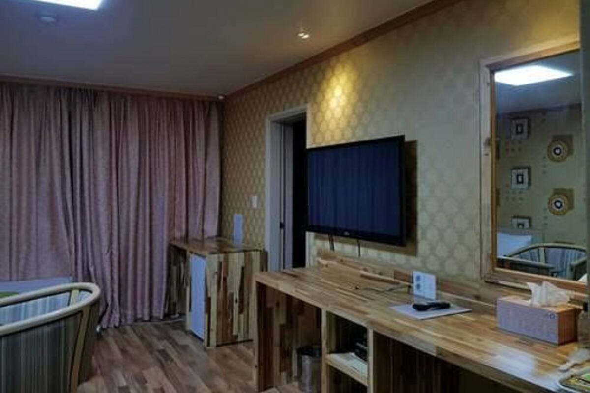 Quarto de hotel com uma secretária de madeira, televisão, espelho grande e janela com cortinas.