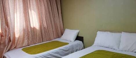 A room with two single beds, each with white bedding and a green accent.