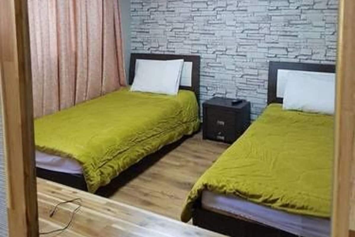Quarto com duas camas, parede com padrão de pedra e piso de madeira.