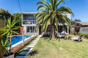 A two-story house with a swimming pool, a covered patio, and a well-maintained lawn.