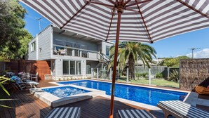 A backyard with a swimming pool, lounge chairs, and a large umbrella.