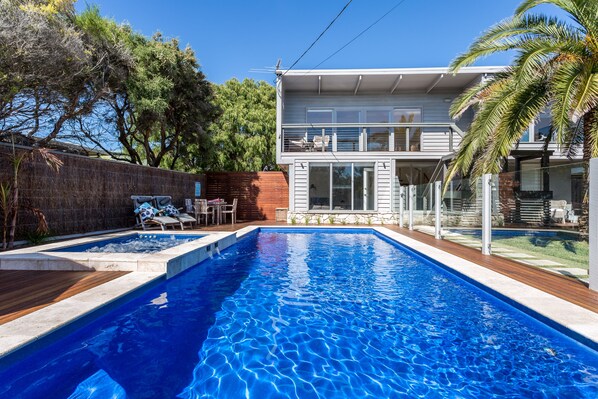 A rectangular swimming pool with a wooden deck, surrounded by a brick wall and trees.