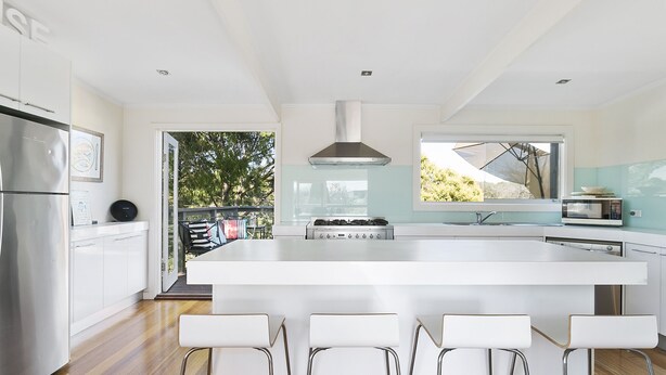 A modern kitchen with a large island, white bar stools, stainless steel appliances, and a view of the outdoors.