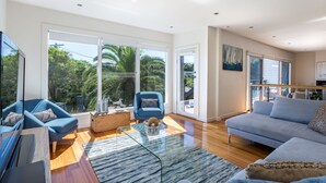A spacious living room with a large window, a blue sofa, a glass coffee table, and a wooden floor.
