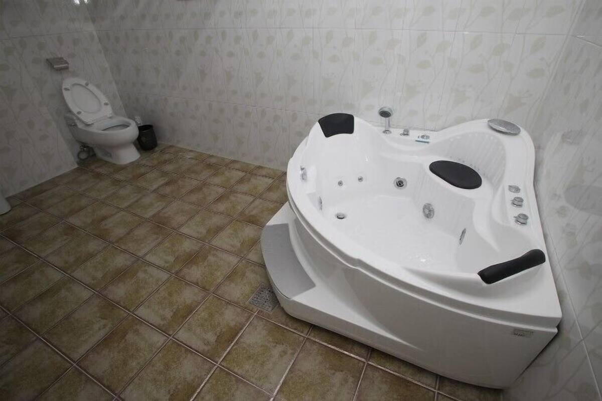 A bathroom with a white bathtub, a toilet, and tiled flooring.
