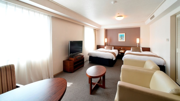 A hotel room with a bed, a TV, a desk, a chair, and a small table. - Alpico Plaza Hotel (Matsumoto)