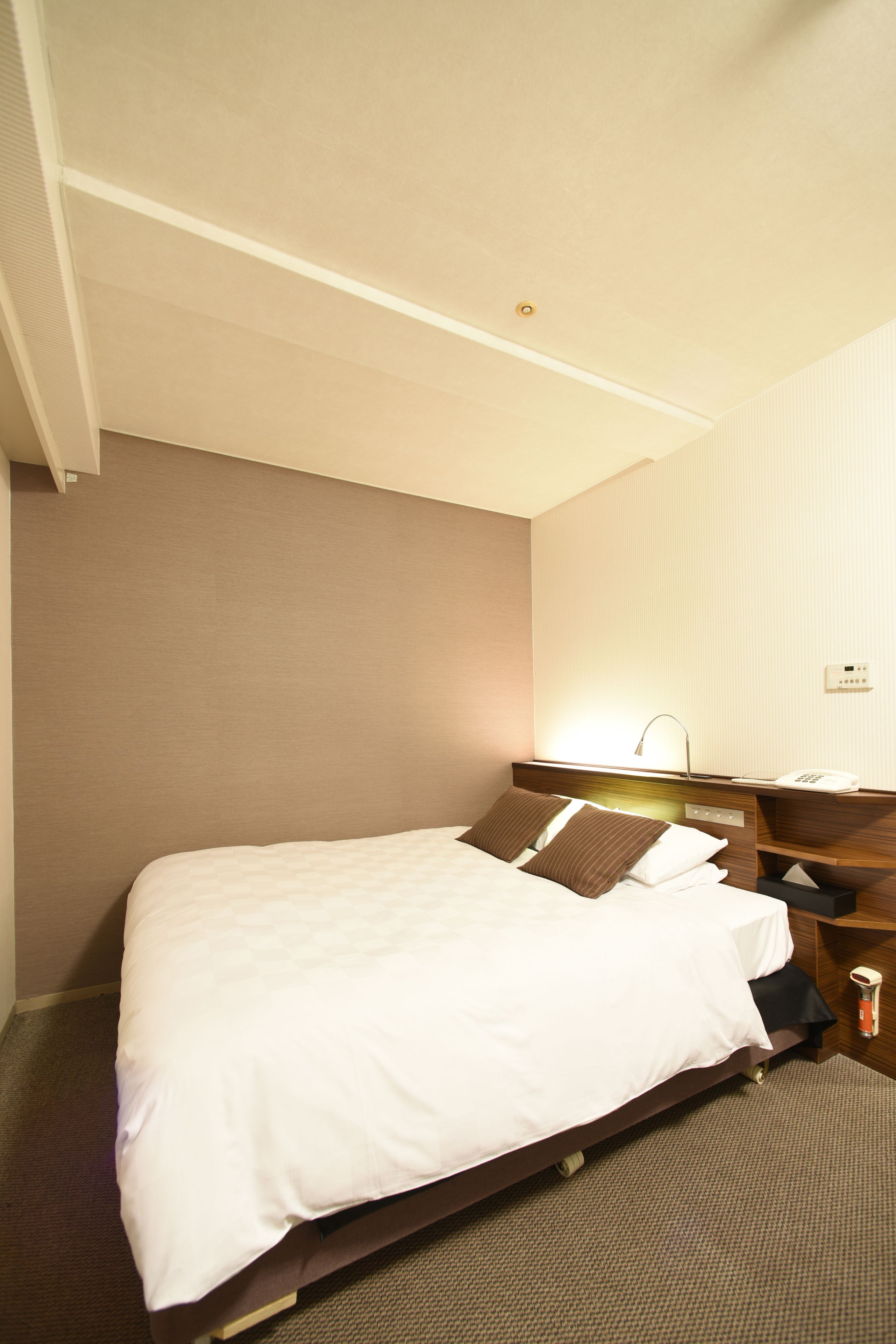 Una habitación de hotel con cama, mesita de noche, lámpara y toma de corriente.