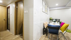 A modern hotel room with a wooden door, a small table with a chair, and a decorative pillow. - Smiley Inn (Kowloon)