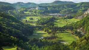 A golf course with a clubhouse, surrounded by lush green hills and a clear sky. - Oak Valley Valley Village (Wonju)