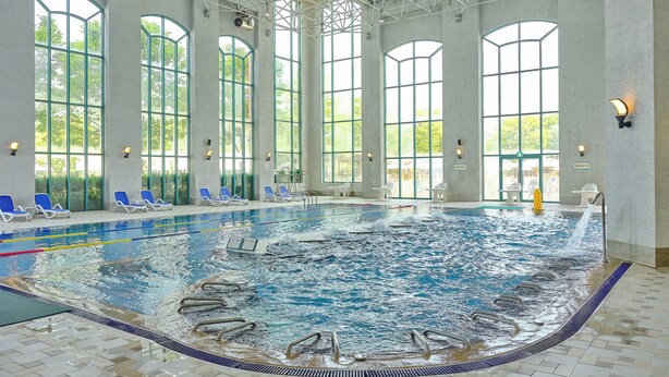 A large indoor swimming pool with clear lanes, sunlit by large windows, and equipped with lounge chairs and a changing room. - Oak Valley Valley Village (Wonju)
