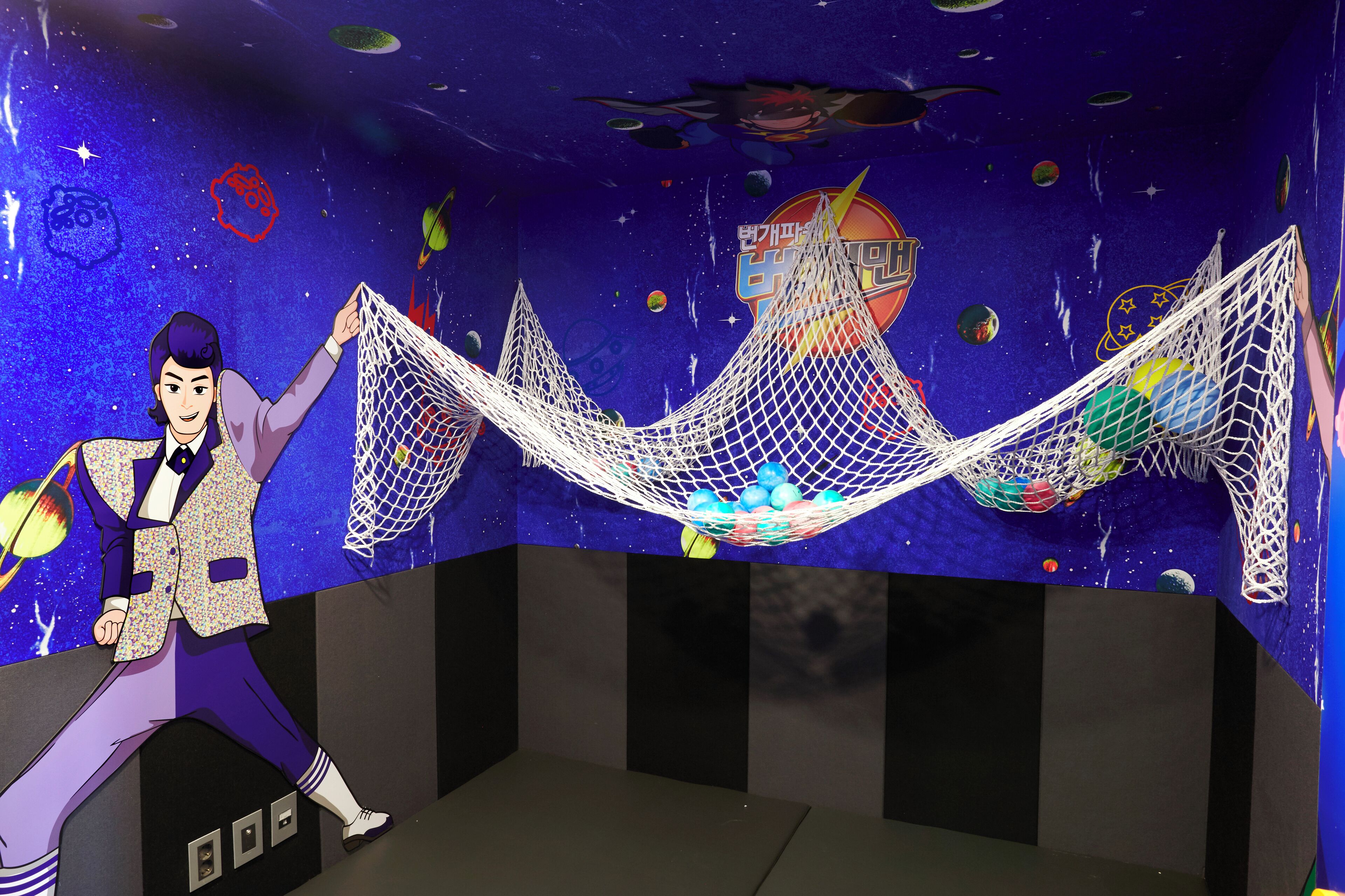 A person in a patterned suit holding a hammock with colorful balls.