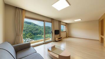 A modern living room with a large window, a sofa, a glass coffee table, and a flat-screen TV.