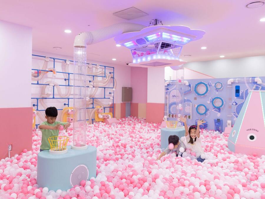 Un espace de jeux pour enfants comprenant une piscine à balles, des structures de jeu et un luminaire au plafond.