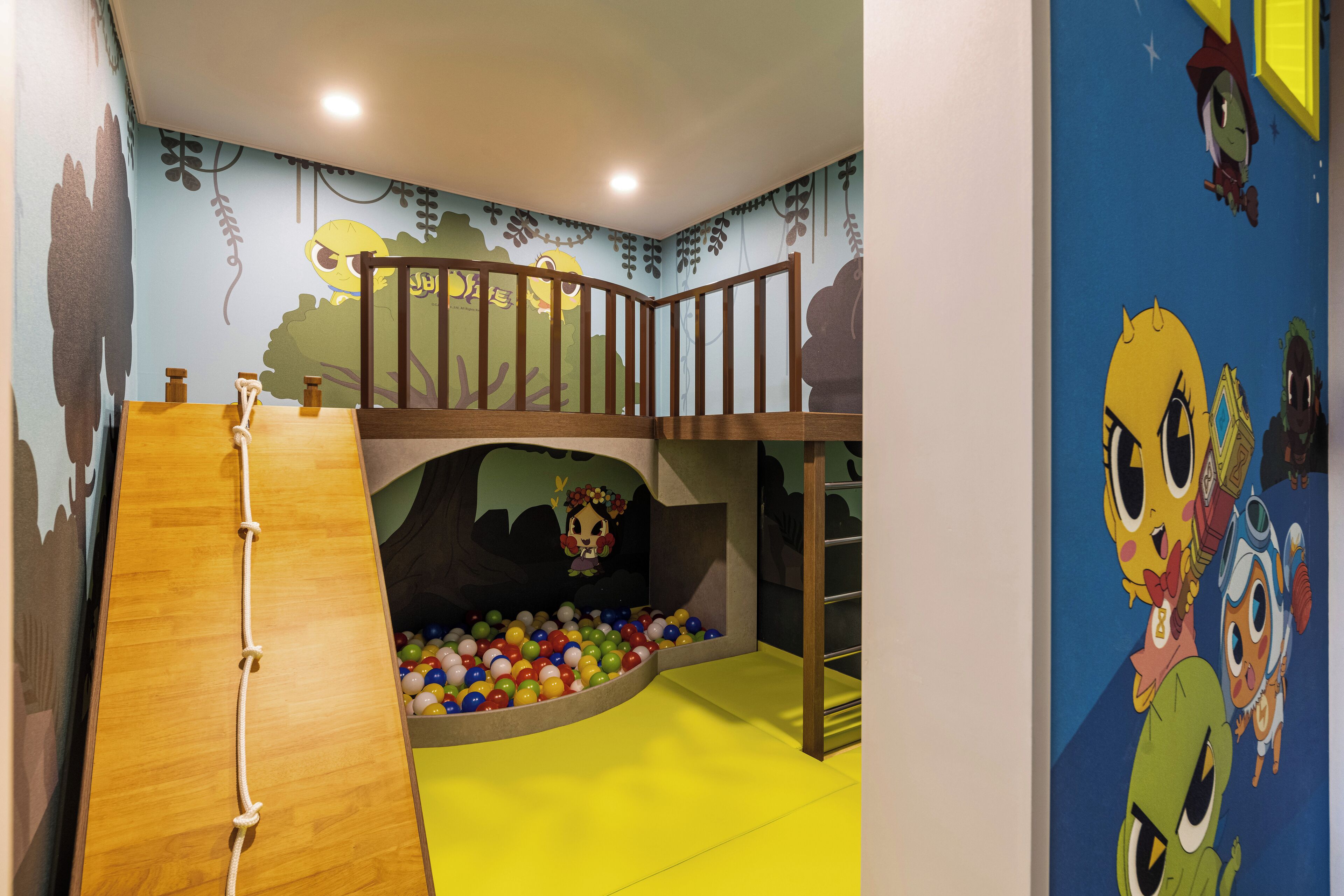 Zona de juegos infantiles con tobogán, piscina de pelotas y decoración de paredes con temática de dibujos animados.
