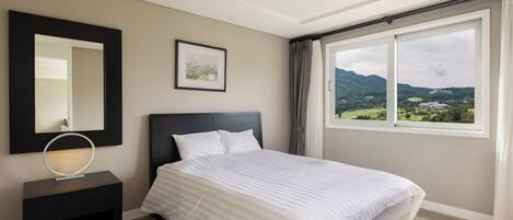 Un dormitorio con cama, mesita de noche, espejo, cuadro enmarco y ventana con vistas a zonas verdes y montañas.