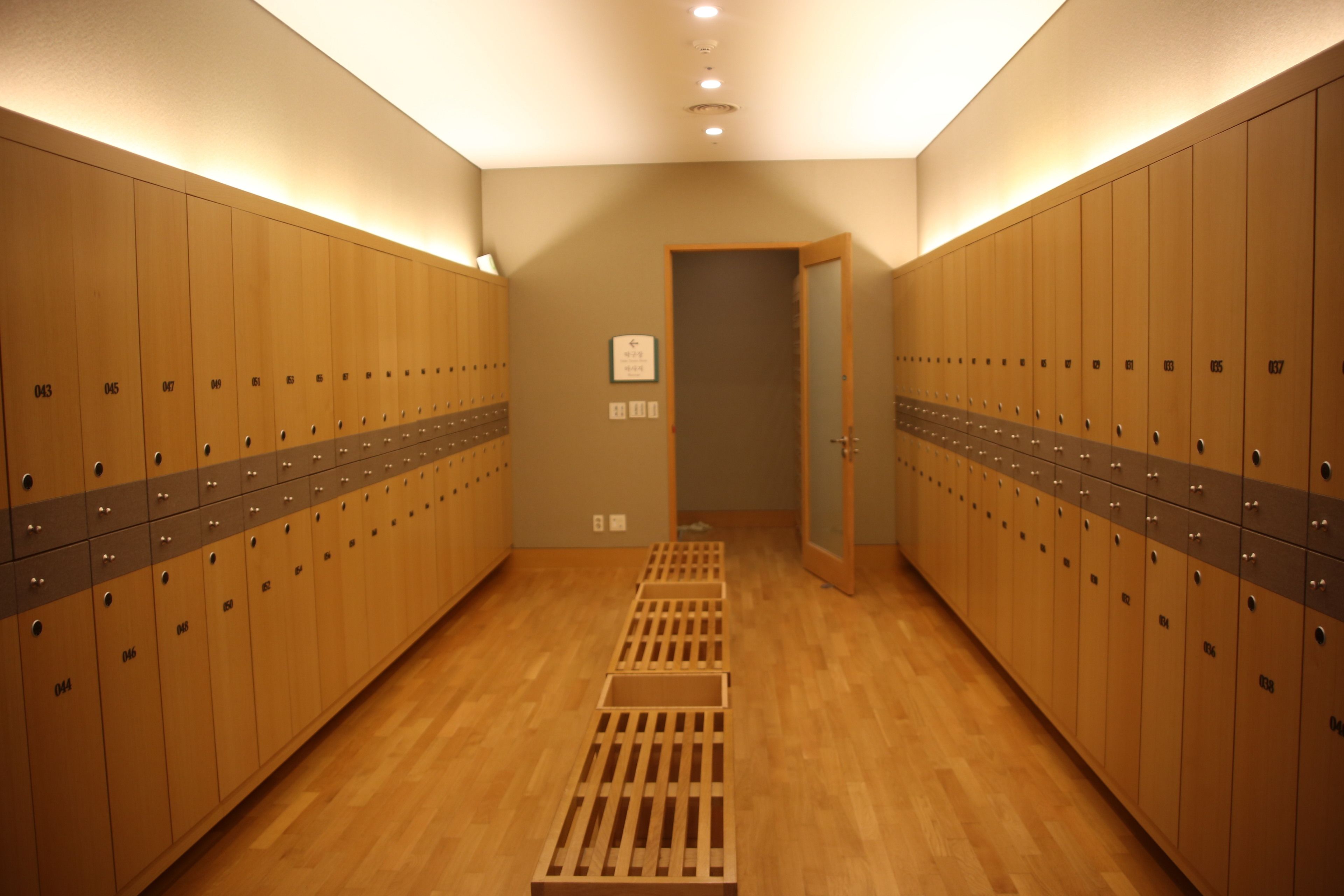 Une rangée de casiers en bois, chacun portant un numéro sur sa porte, un plancher en bois et une porte au bout de la rangée.
