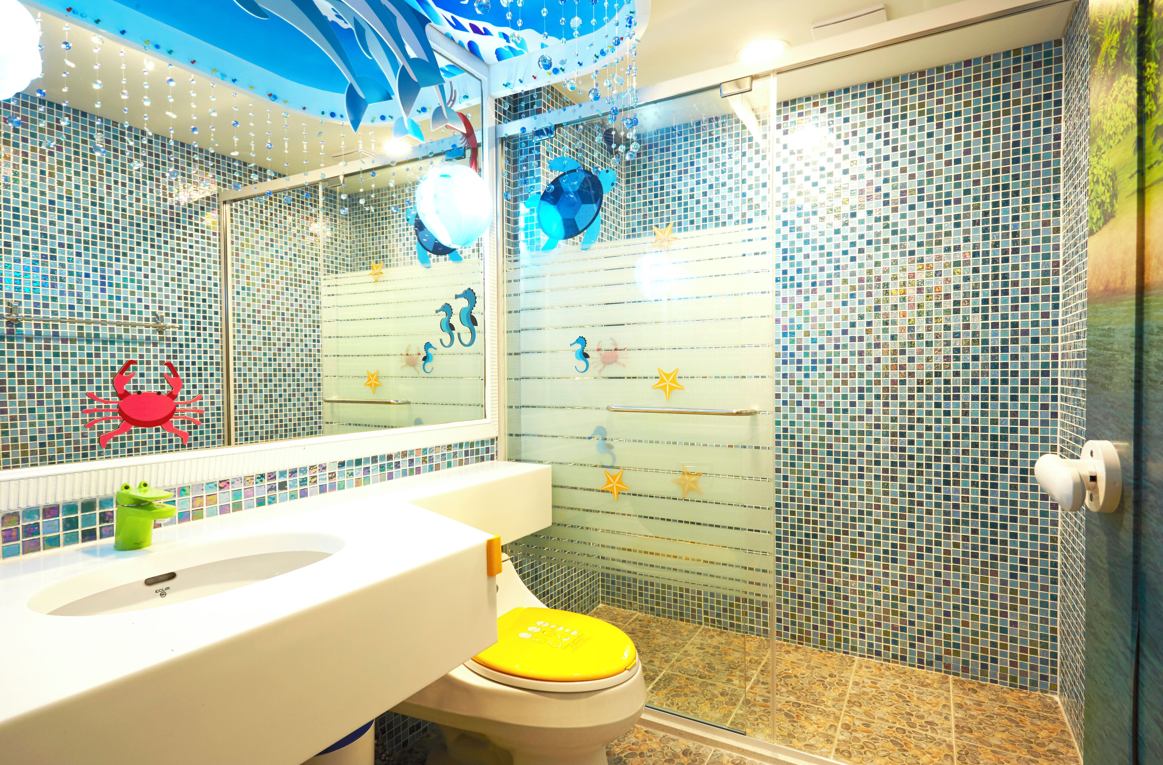 A bathroom with a white sink, a yellow toilet, and a glass shower enclosure with mosaic tiles.