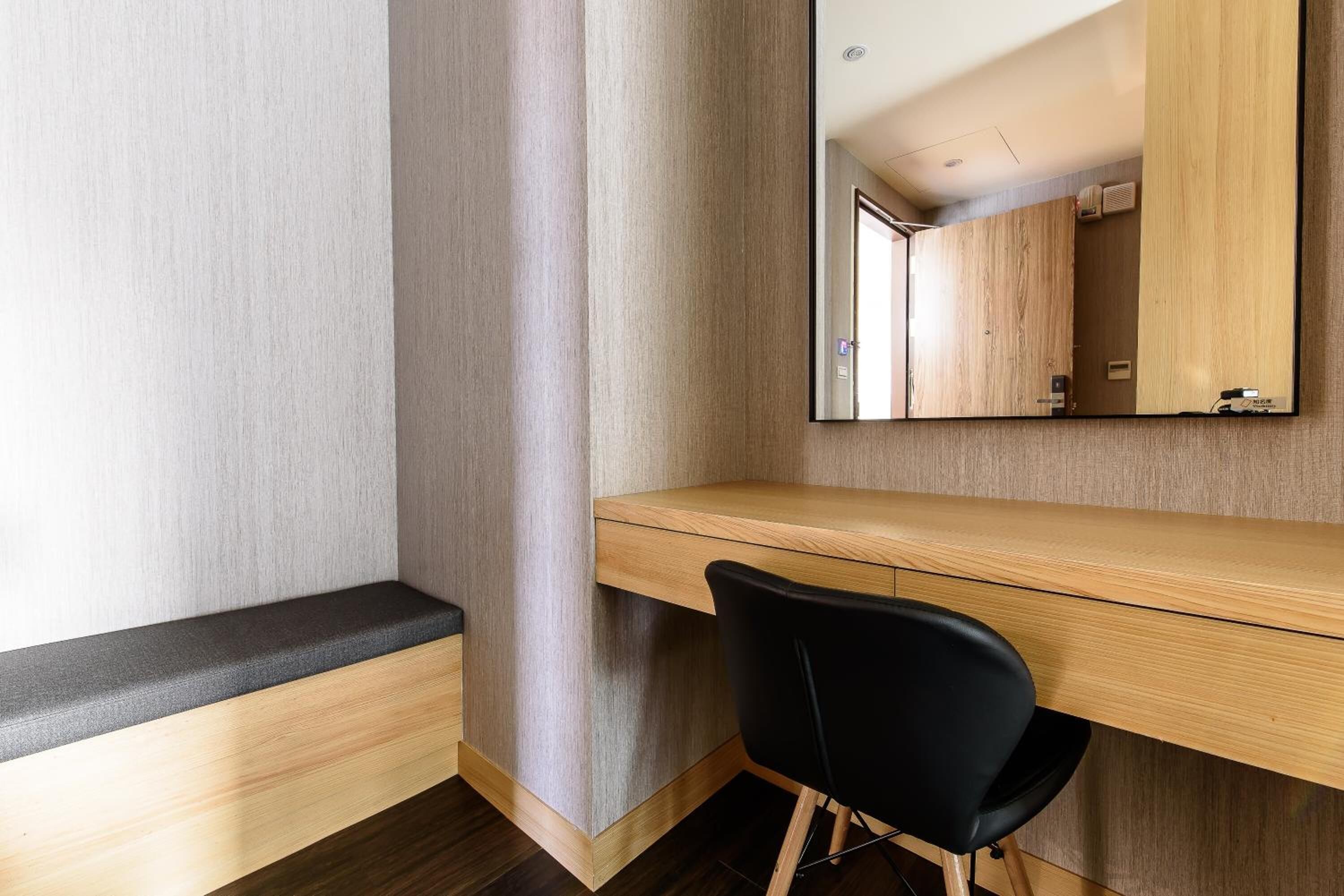 Ein modernes Zimmer mit Schreibtisch aus Holz, schwarzem Stuhl und einem großen Spiegel.