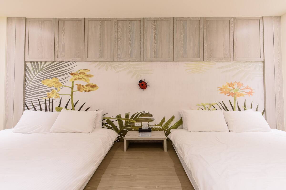 Quarto com duas camas de solteiro, uma mesa de cabeceira com abajur e um objeto vermelho fixado na parede.