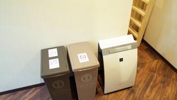 Three trash bins and a white appliance, likely a coffee machine, in a hallway with wooden flooring and a white wall.