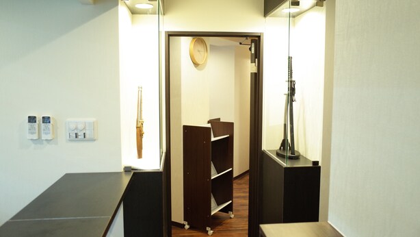 A hallway with a wooden floor, a clock on the wall, and a small wooden shelf unit. - bnb+ Shinjuku Castle - Hostel (Tokyo)