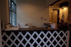 A reception desk with a black and white patterned partition, a window, and a mounted sculpture. - bnb+ Shinjuku Castle - Hostel (Tokyo)