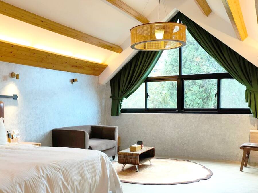 A bedroom with a large bed, a wooden ceiling, a window with curtains, and a small table.