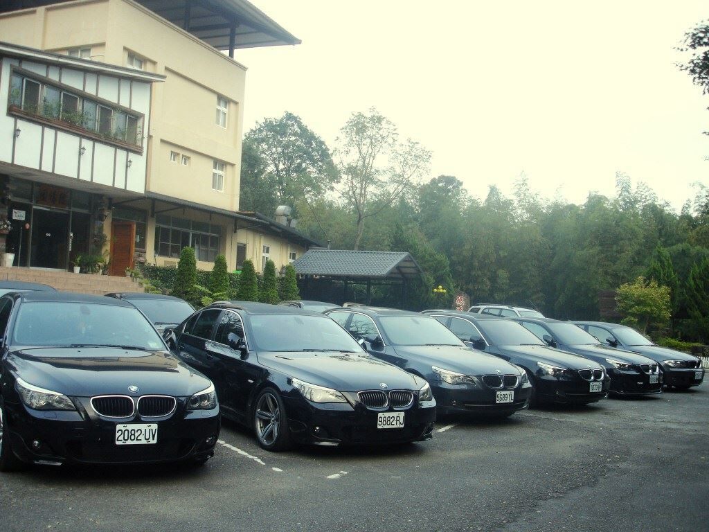 A row of black BMW cars parked in front of a building with a modern architectural style, featuring large windows and a flat roof.