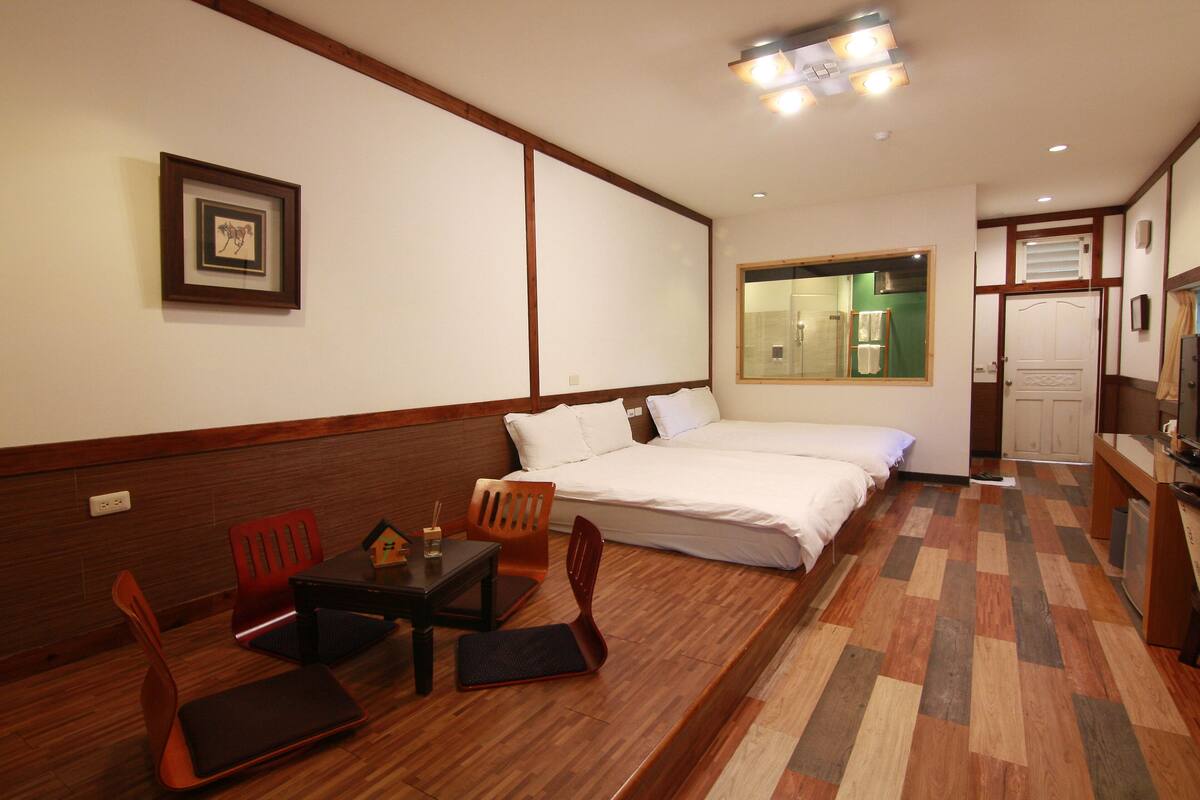 A hotel room with a bed, a desk with chairs, a small table with a glass, and a framed picture on the wall.